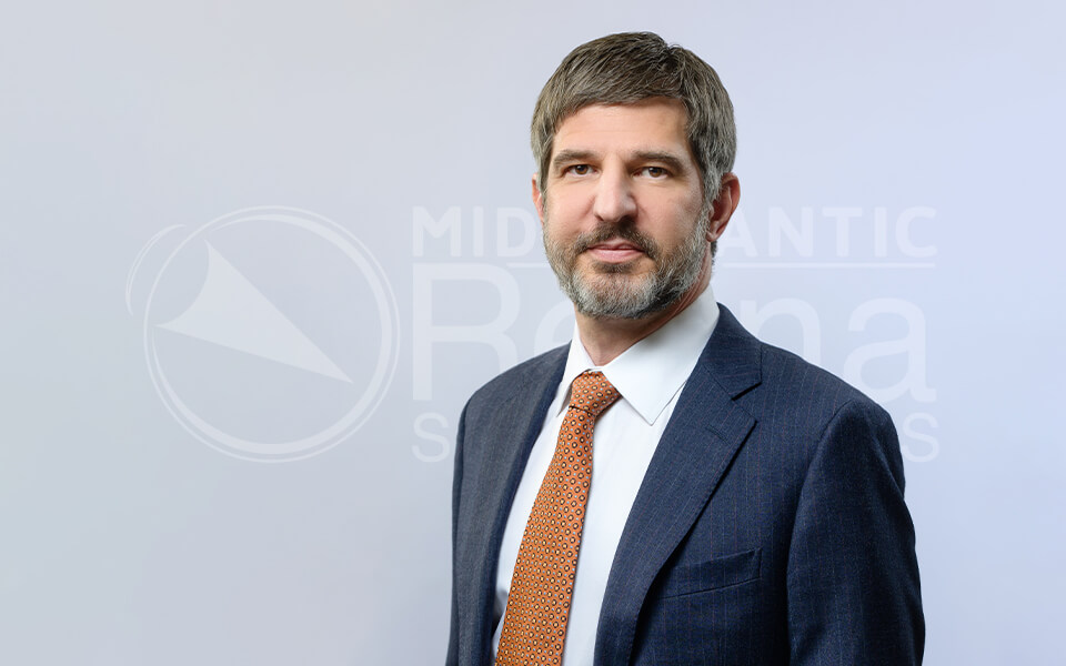 Man in a suit with orange tie posing in front of a Mid Atlantic Retina backdrop.