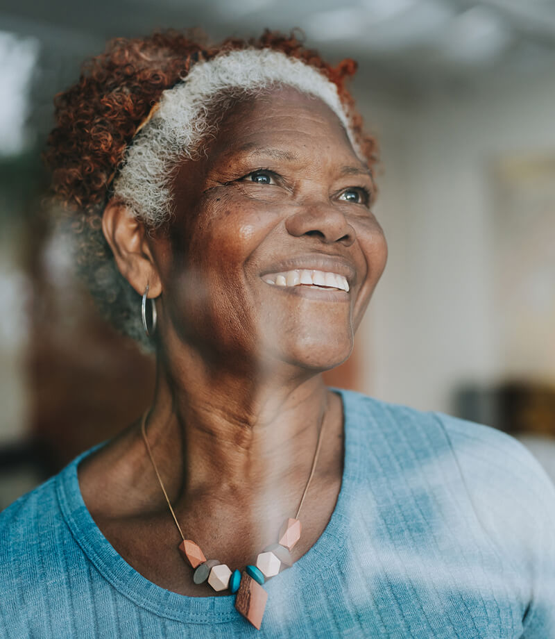 Smiling elderly woman with curly hair and necklace looking off to the side.