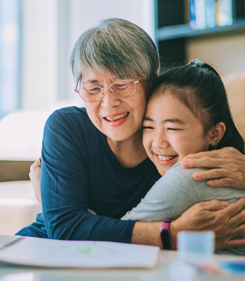 Elderly woman and young girl smiling and hugging each other warmly.