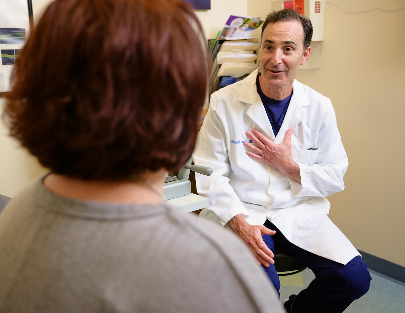 Doctor in white coat consulting with a seated patient in an exam room.