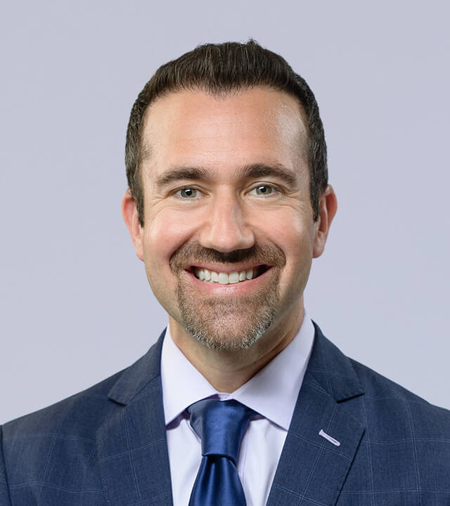 Smiling man in a blue suit and tie, professional headshot.