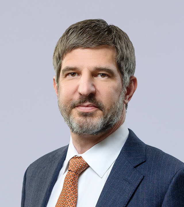 Professional headshot of a man in a suit with a light background.
